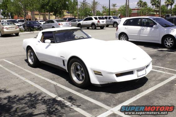 White sports car parked in a lot, front quarter view. Appears to be a C3 Corvette