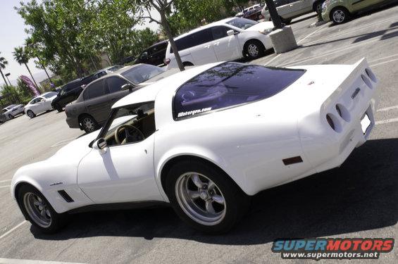 White Chevrolet Corvette C3 coupe with aftermarket wheels, seen from the 3/4 front angle in a parking lot