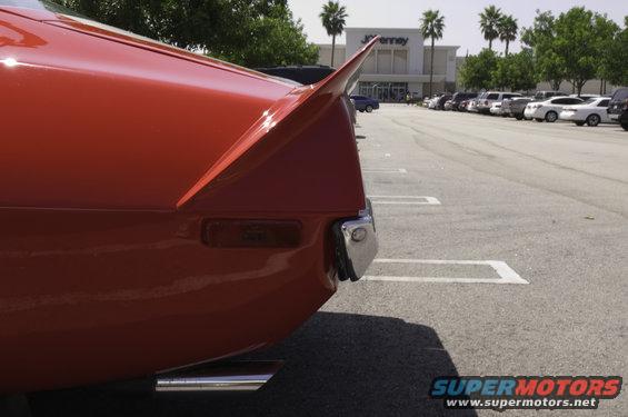 Red car tail fin with chrome bumper and exhaust pipe, parked in a lot with other vehicles