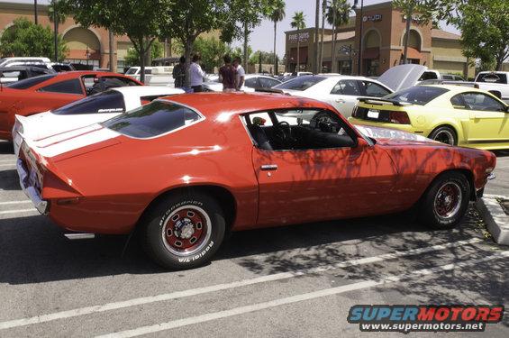 Red 1970s muscle car with white racing stripes on rear deck, side view