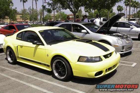 Yellow Ford Mustang with black racing stripes and black rims parked in a lot