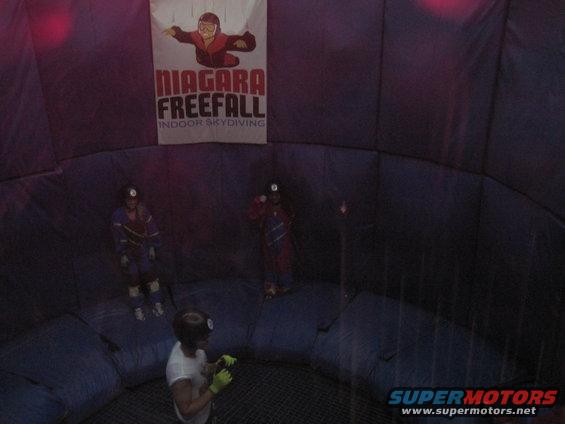 People in jumpsuits inside a wind tunnel with a 'Niagara Freefall' banner