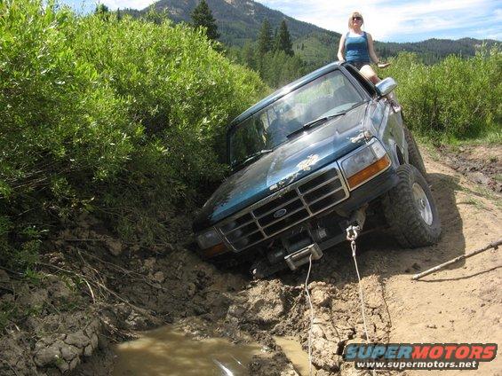 Blue Ford Bronco stuck in mud, angled front view, winch attached