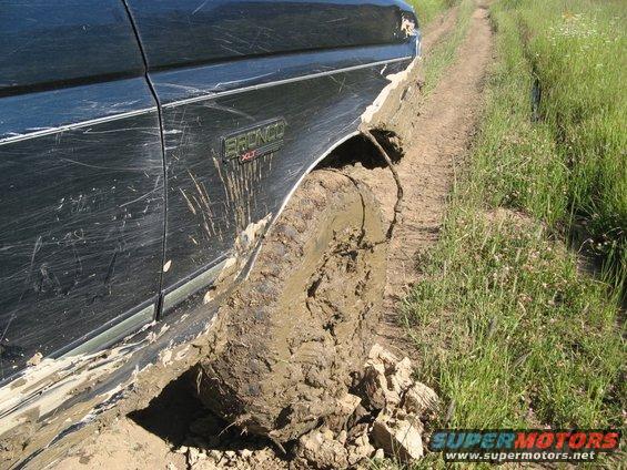 Side view of a 1995 Ford Bronco's front fender and wheel stuck deep in mud on a dirt track