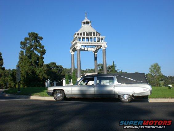 Silver 1972 Cadillac Fleetwood hearse parked by a mausoleum