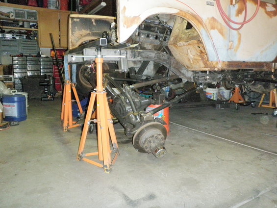Vehicle chassis on jack stands, showing suspension and frame work. Some body panels are visible