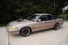 1993 Ford Crown Victoria - A tan sedan with a prominent hood scoop and aftermarket wheels is parked on a concrete driveway.