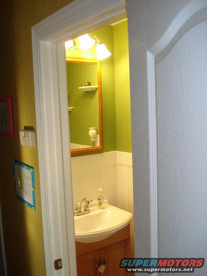 Bathroom sink with wood vanity cabinet, mirror, and light fixture above. Walls are green and white