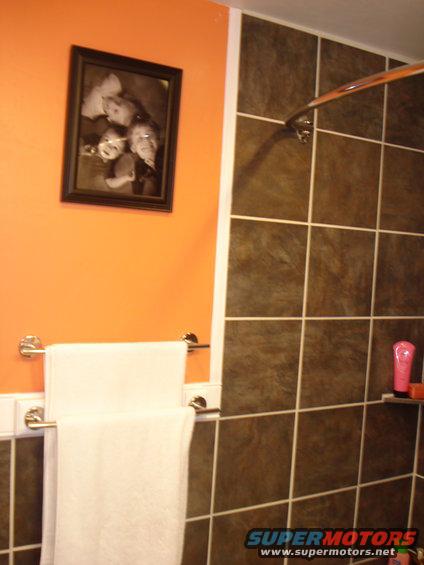 Framed black and white photo of children on orange wall above towels in bathroom