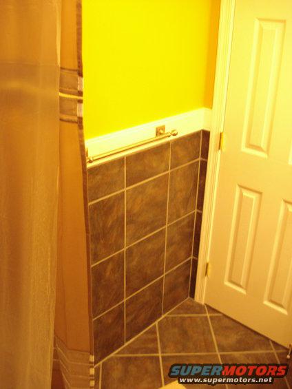 Bathroom corner with yellow wall, dark tiled walls, tiled floor, and a white door