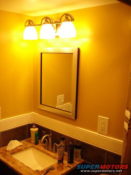 Yellow bathroom vanity with sink, mirror, and triple light fixture