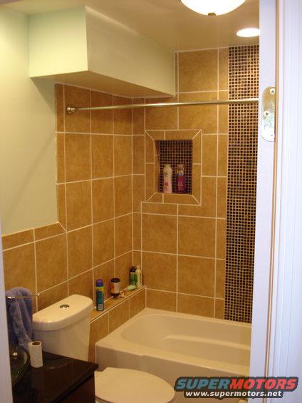 Bathroom with tan tile, toilet, and bathtub. Shower rod and bottles of shampoo visible