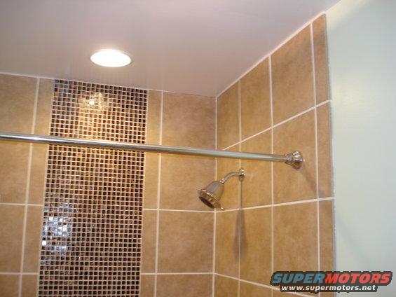 Shower head and chrome rod against tan tiled wall with mosaic accent