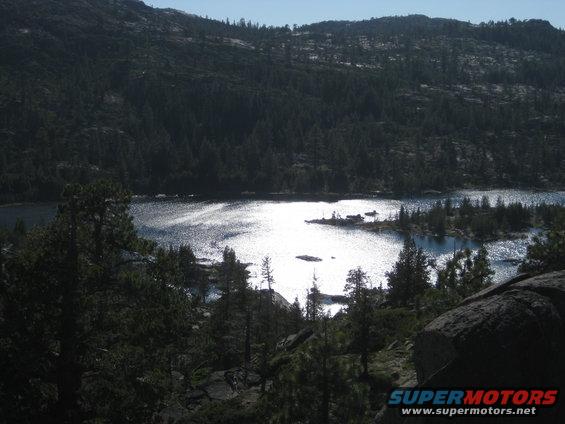 Lake reflecting sunlight, surrounded by pine trees and mountains