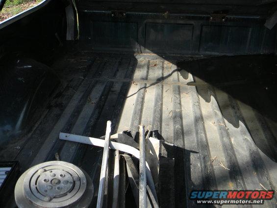 Truck bed interior with some metal parts and a round component. Sunlight casts shadows