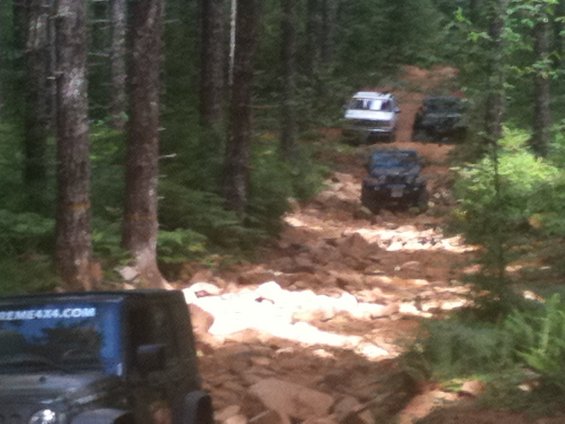 Jeeps driving on a rough, rocky trail through a forest. One Jeep in the foreground has "EXTREME4X4.COM" on its side