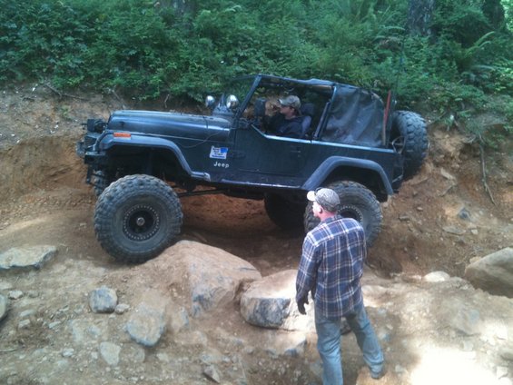 Dark green Jeep Wrangler navigating a rocky off-road trail with a person standing nearby