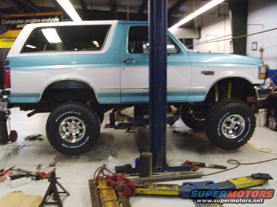 Side view of a 1994 Ford Bronco on a car lift, showing its lifted suspension and two-tone paint job
