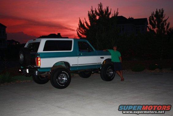 1994 Ford Bronco with a person leaning on the front fender at dusk