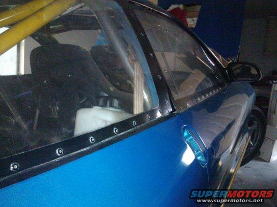 Blue custom car interior with yellow roll cage, clear plastic windows riveted on, and a white fluid tank visible
