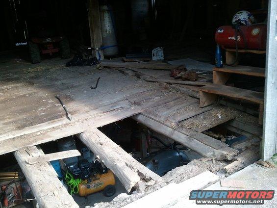 broken wooden floorboards in a dark barn, with an air compressor and other items visible below