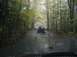 1986 Ford Bronco - A dark SUV navigates a muddy path through a dense forest during autumn.