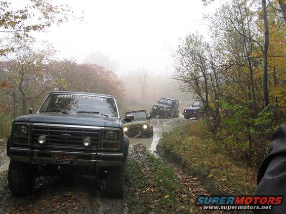 Front view of a dark blue SUV on a muddy trail with other vehicles behind