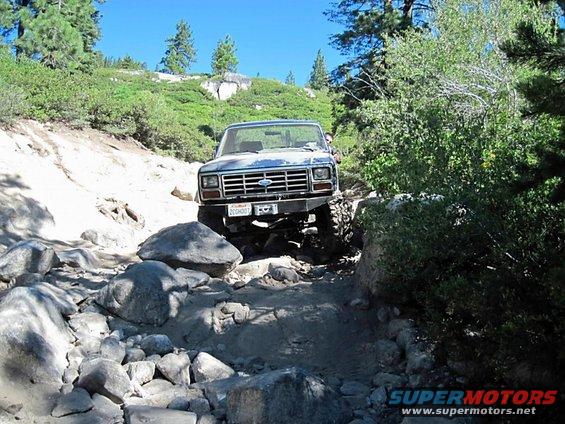 Blue 1980s Ford Bronco navigating a rocky off-road trail