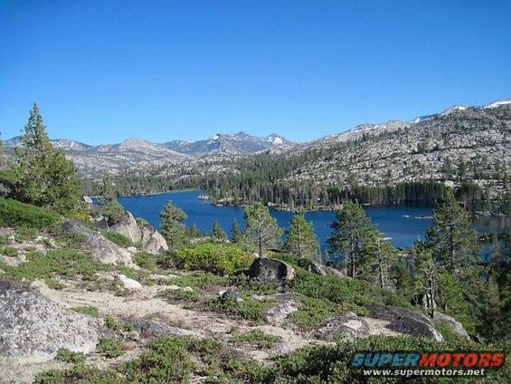 Mountain landscape with a blue lake surrounded by pine trees and rocky terrain under a clear blue sky