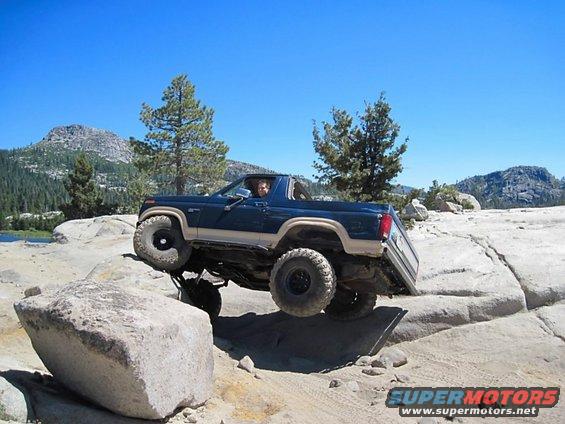 Blue off-road SUV with lifted suspension driving over rocks