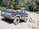 1986 Ford Bronco - A blue Ford Bronco navigates a challenging rocky terrain on a sunny day.