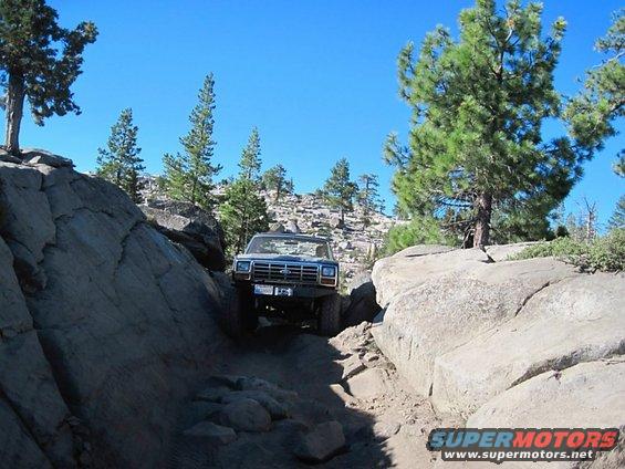 Blue SUV navigating a narrow, rocky trail between large boulders