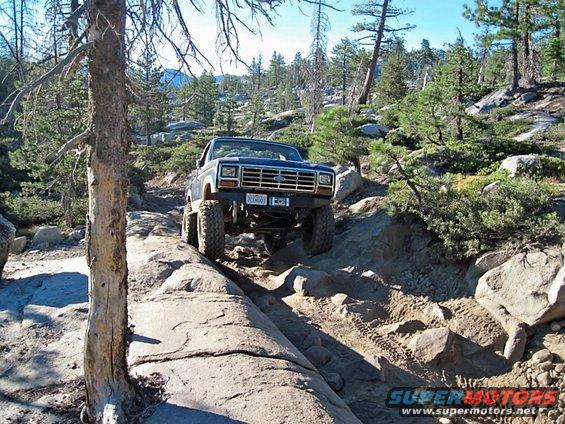 1980 Ford Bronco navigating a steep, rocky off-road trail with large tires and lifted suspension. License plate reads '205001'