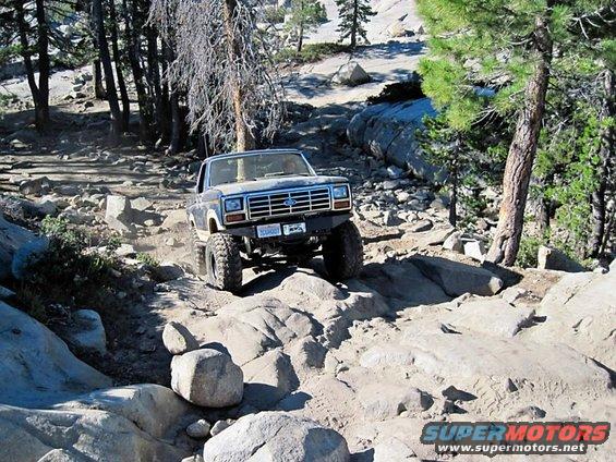 Ford Bronco climbing over rocks on a trail. License plate visible