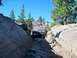 1986 Ford Bronco - Ford Bronco tackling a challenging rocky trail in a mountainous, wooded area under a clear blue sky.