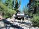 1986 Ford Bronco - This 1980s Ford Bronco is shown off-roading on a challenging, boulder-strewn path through a forest.