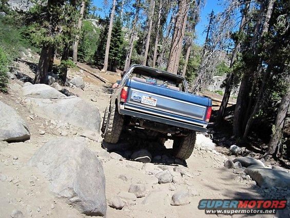 1986 Ford Bronco navigating a boulder-strewn mountain path, rear view