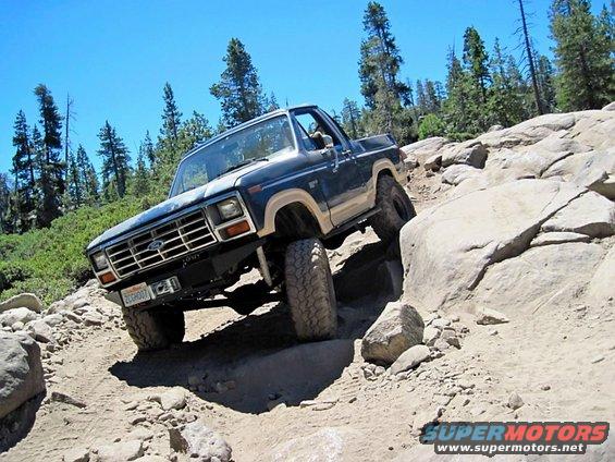 Blue and tan 1986 Ford Bronco navigating a steep, rocky incline