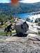 1986 Ford Bronco - Man attempts to move a large boulder on a rocky terrain overlooking a scenic lake and forest.
