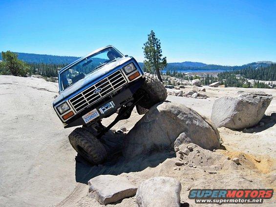 Ford Bronco climbing over rocks on a dirt trail with a lake in the background