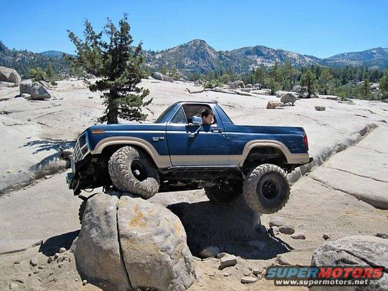 Blue and tan 1986 Ford Bronco navigating rocky terrain with one wheel off the ground