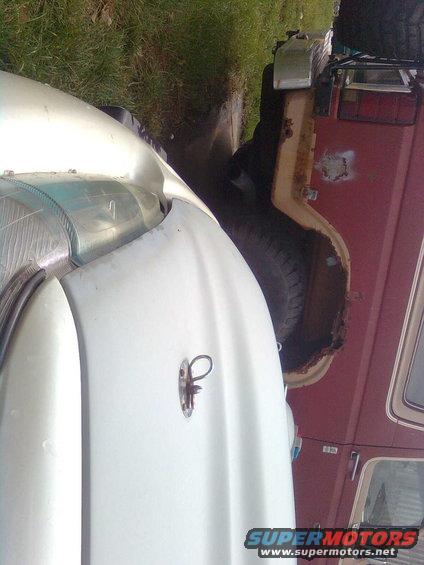 Close-up of a white vehicle's fender next to a red vehicle's side, showing rust and a spare tire
