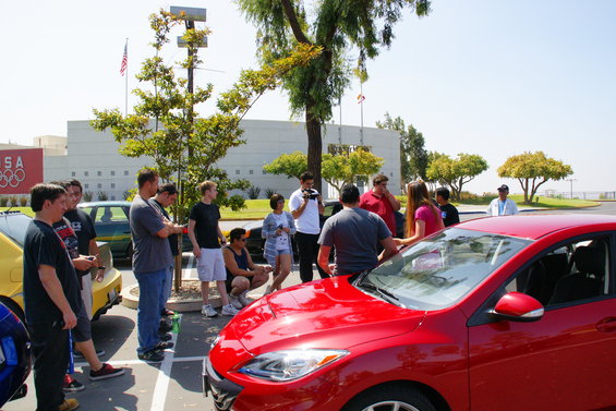 Red car parked in a lot with people gathered around
