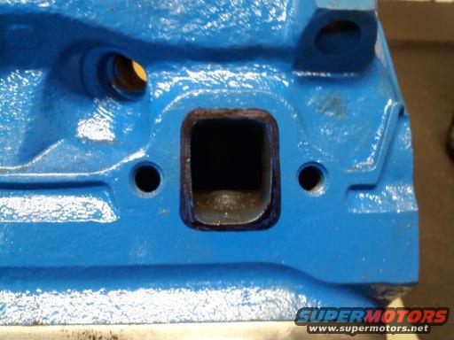 Blue engine block part with rectangular intake port and two bolt holes