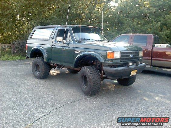 Green lifted 1989 Ford Bronco parked next to a maroon pickup truck