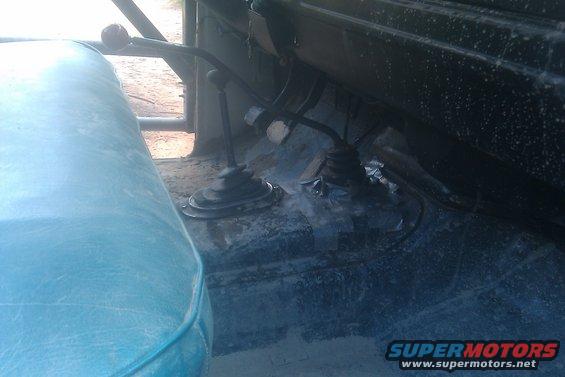 Vehicle interior showing two black gear shifters and a blue seat. The floor is dusty