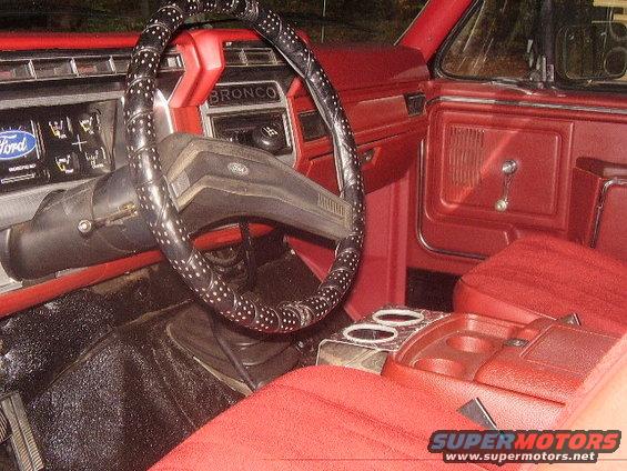 Interior of a 1986 Ford Bronco with red seats and dashboard, showing the steering wheel and center console