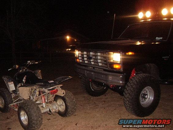 Black pickup truck with off-road tires and lights next to a muddy ATV