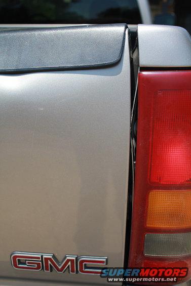 Close-up of a silver GMC pickup truck's tailgate and taillight. GMC logo visible
