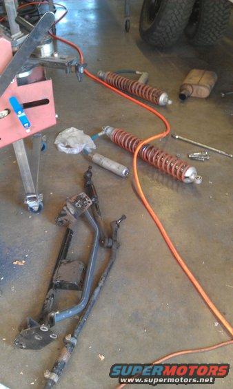Suspension parts, including shocks and springs, laid out on a garage floor next to tools and an air hose